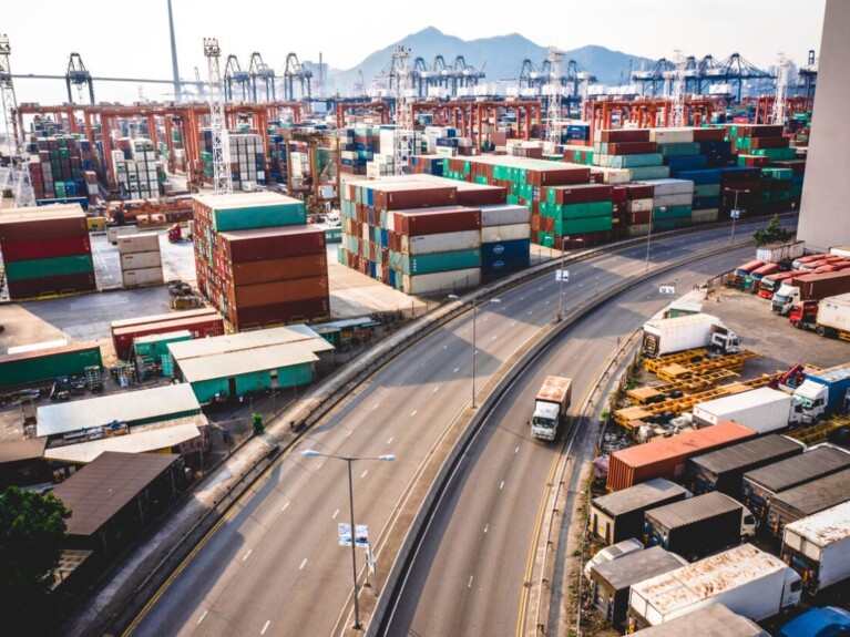 Shipping containers and trucks by a highway.