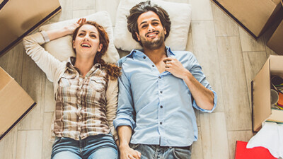 A man and a woman lying on the floor, surrounded by moving boxes.