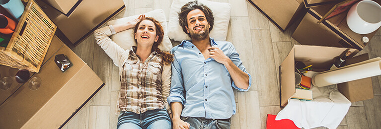 A man and a woman lying on the floor, surrounded by moving boxes.