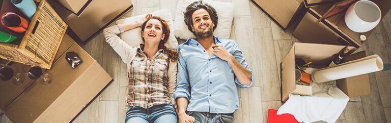 A man and a woman lying on the floor, surrounded by moving boxes.