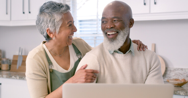 An older couple smiling in front of a computer.