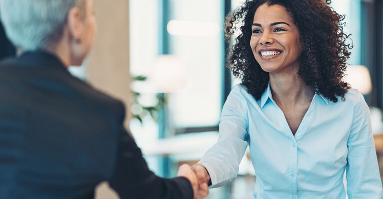 Two women smiling and shaking hands.