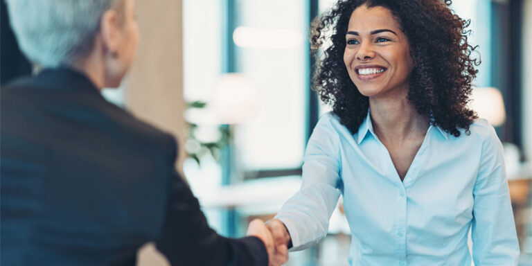 Two women smiling and shaking hands.