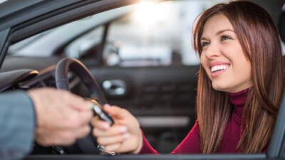 Woman in new car, accepting car keys from car salesman.
