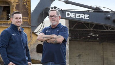 Two men in front of construction equipment.