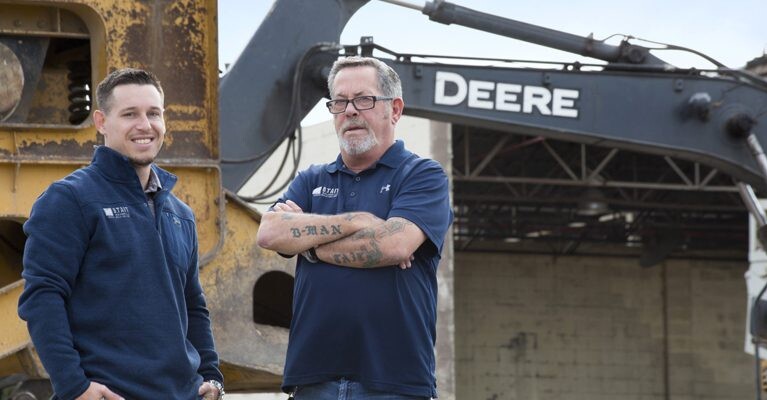 Two men in front of construction equipment.