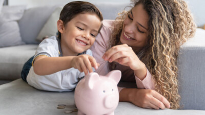 Child and woman putting coins into a piggy bank.