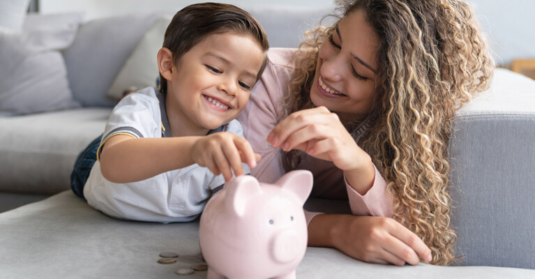 Child and woman putting coins into a piggy bank.