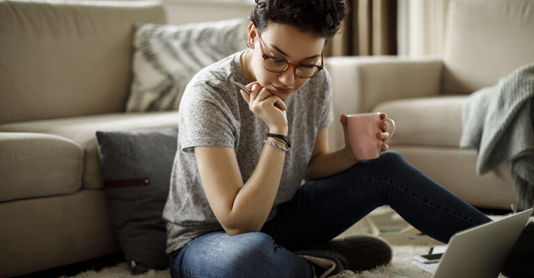 A student doing homework while holding a pink mug.