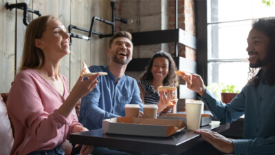 Two women and two men sitting at a restaurant table, eating pizza.