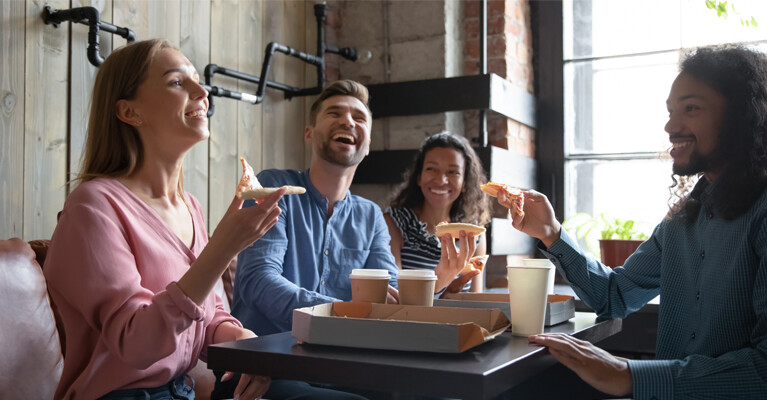 Two women and two men sitting at a restaurant table, eating pizza.