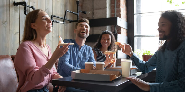 Two women and two men sitting at a restaurant table, eating pizza.