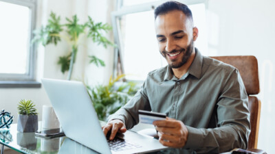 A man using a laptop while holding his credit card.