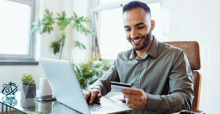 A man using a laptop while holding his credit card.