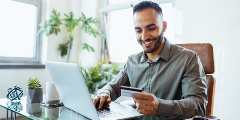A man using a laptop while holding his credit card.