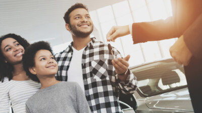 Man, woman, and child accepting car keys from car salesman.