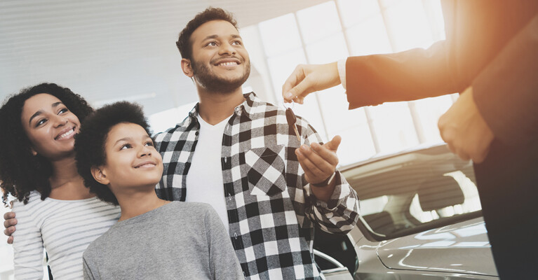 Man, woman, and child accepting car keys from car salesman.