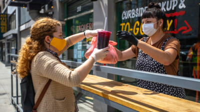 Food service worker handing a curbside to-go order of food to a customer.