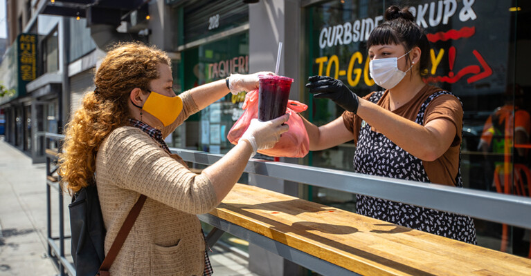 Food service worker handing a curbside to-go order of food to a customer.