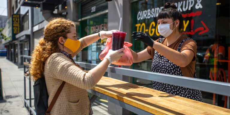 Food service worker handing a curbside to-go order of food to a customer.