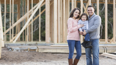 Woman, child, and man in front of home in construction.