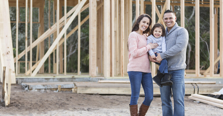 Woman, child, and man in front of home in construction.