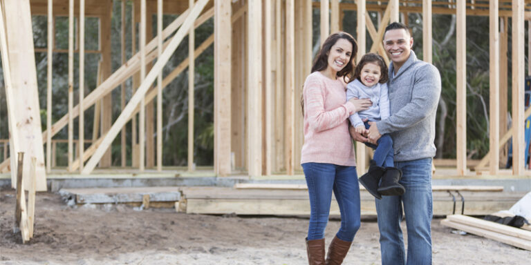 Woman, child, and man in front of home in construction.