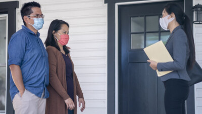 A real estate agent meeting a couple in front of a house.