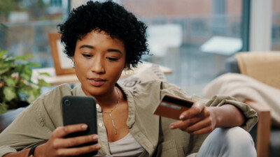 A woman using her cell phone and holding a credit card.