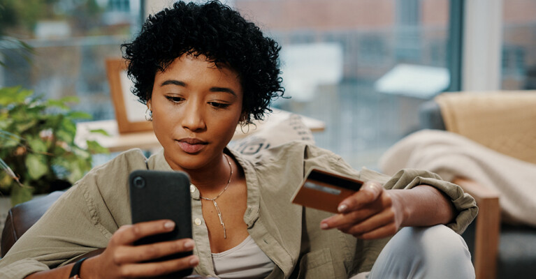 A woman using her cell phone and holding a credit card.