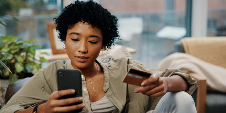 A woman using her cell phone and holding a credit card.