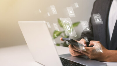 A person using a laptop and smartphone with security icons.