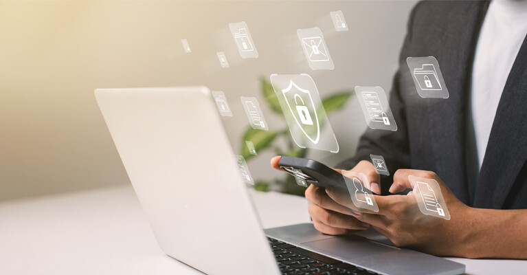 A person using a laptop and smartphone with security icons.