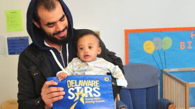A man and his child holding a banner that reads: "Delaware Stars. Young stars. Shining futures."