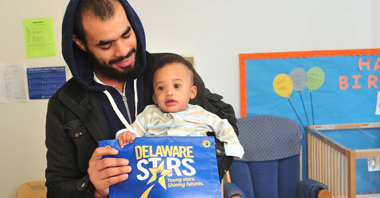 A man and his child holding a banner that reads: "Delaware Stars. Young stars. Shining futures."