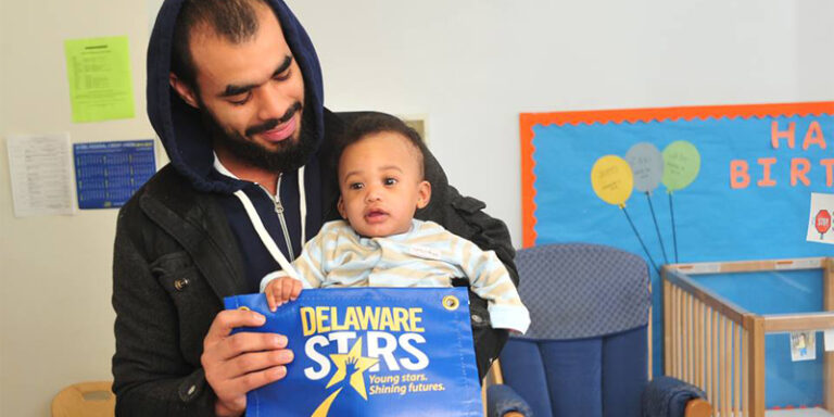 A man and his child holding a banner that reads: "Delaware Stars. Young stars. Shining futures."