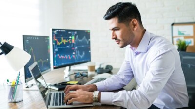 Man using laptop computer, with stock charts on monitors.