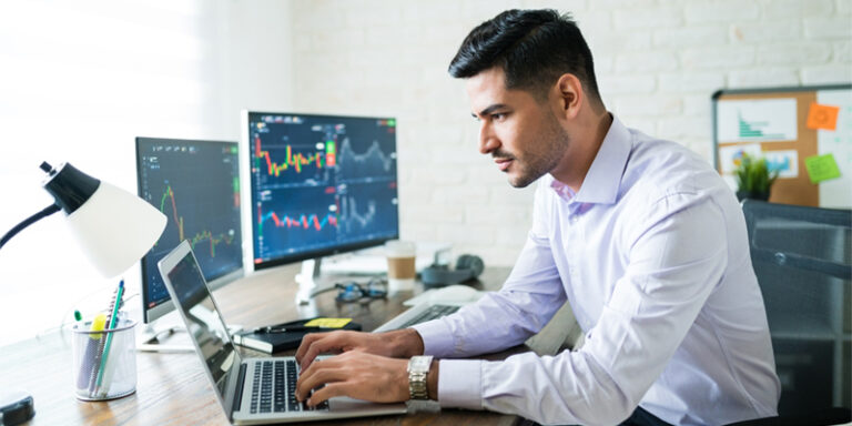 Man using laptop computer, with stock charts on monitors.