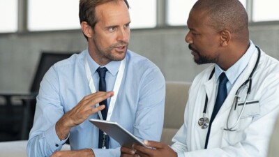 Two men conversing and holding a tablet.