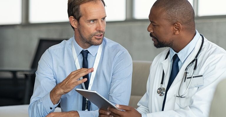 Two men conversing and holding a tablet.