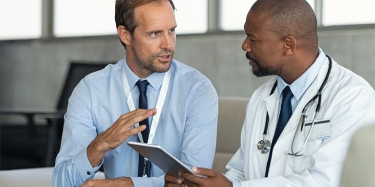 Two men conversing and holding a tablet.