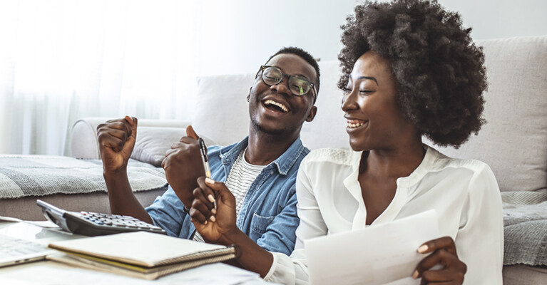 A man and a woman smiling while calculating their finances.