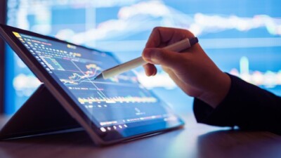 Hand using a tablet and stylus to track stocks.