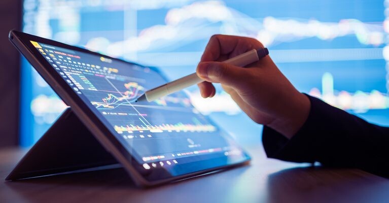 Hand using a tablet and stylus to track stocks.