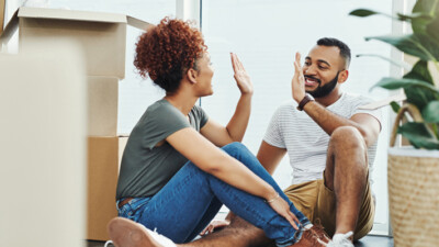 A man and a woman high-fiving each other, surrounded by moving boxes.