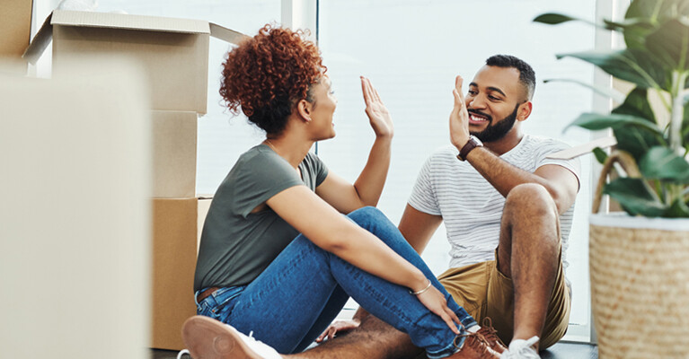 A man and a woman high-fiving each other, surrounded by moving boxes.