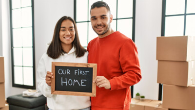 Two people holding a chalkboard that reads "Our First Home."