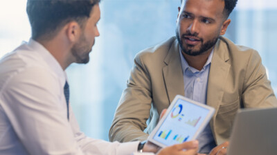 A businessman and a customer reviewing charts on a tablet screen.