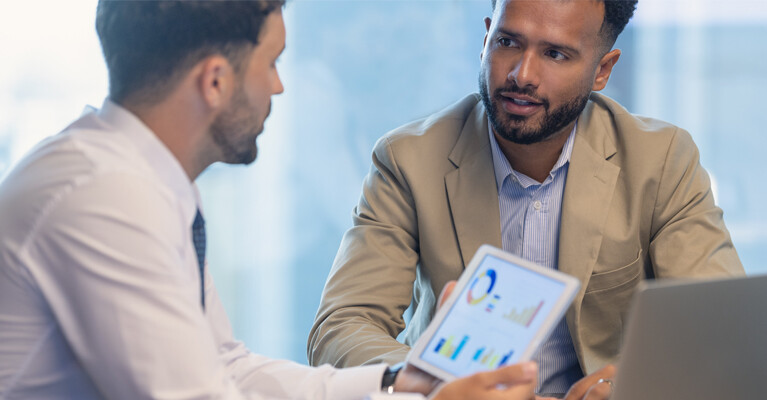 A businessman and a customer reviewing charts on a tablet screen.