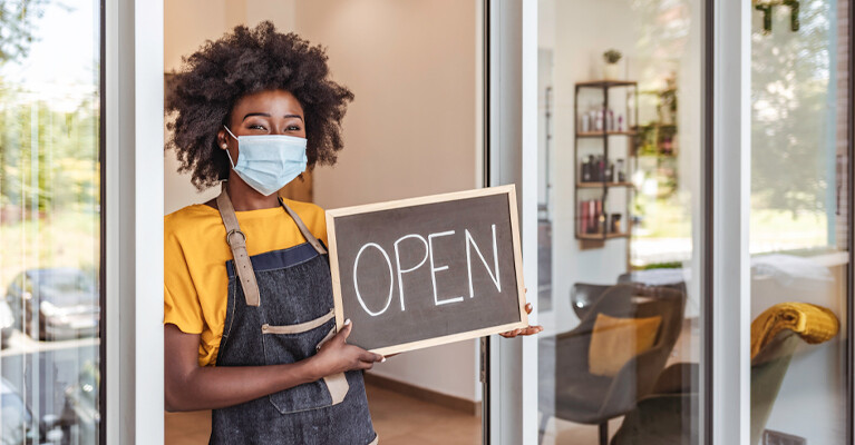 A business owner holding an "Open" sign in the front doorway of their business.